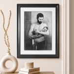 Charcoal drawing of a bearded father standing in a doorway holding his sleeping baby across his forearms
