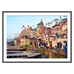 Photograph of bathers in the Ganga at Varanasi with moored boats, ghat steps and temple spires in morning light
