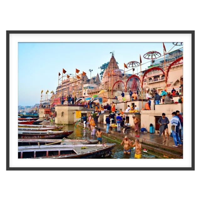 Photograph of bathers in the Ganga at Varanasi with moored boats, ghat steps and temple spires in morning light