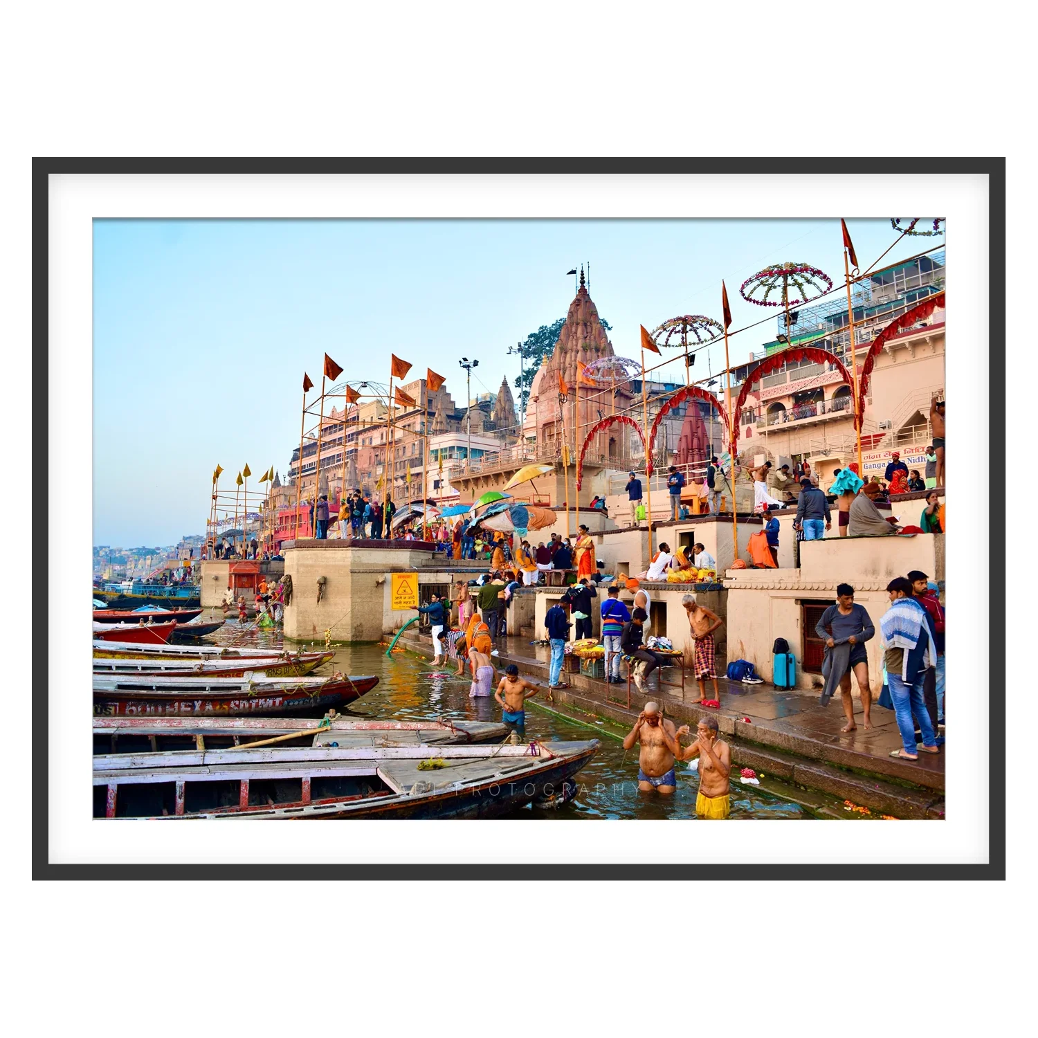 Photograph of bathers in the Ganga at Varanasi with moored boats, ghat steps and temple spires in morning light